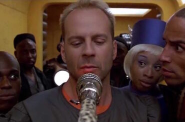 Fictional character Corbin Dallas from the movie The Fifth Element looking at a microphone surrounded by Ruby Rhod's entourage